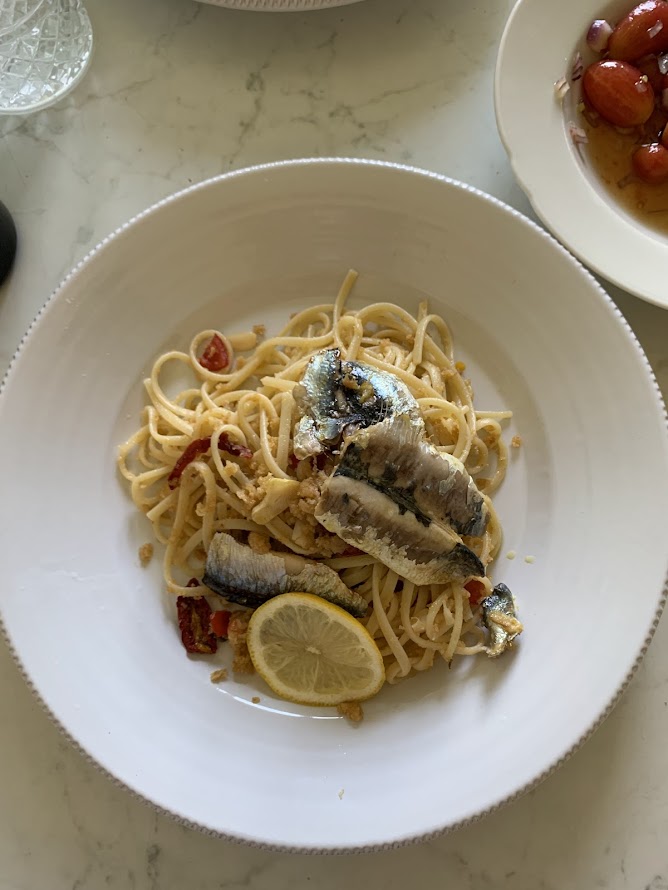 Plate of spaghetti with sardines, lemon slice, and tomatoes, served on a white dish.