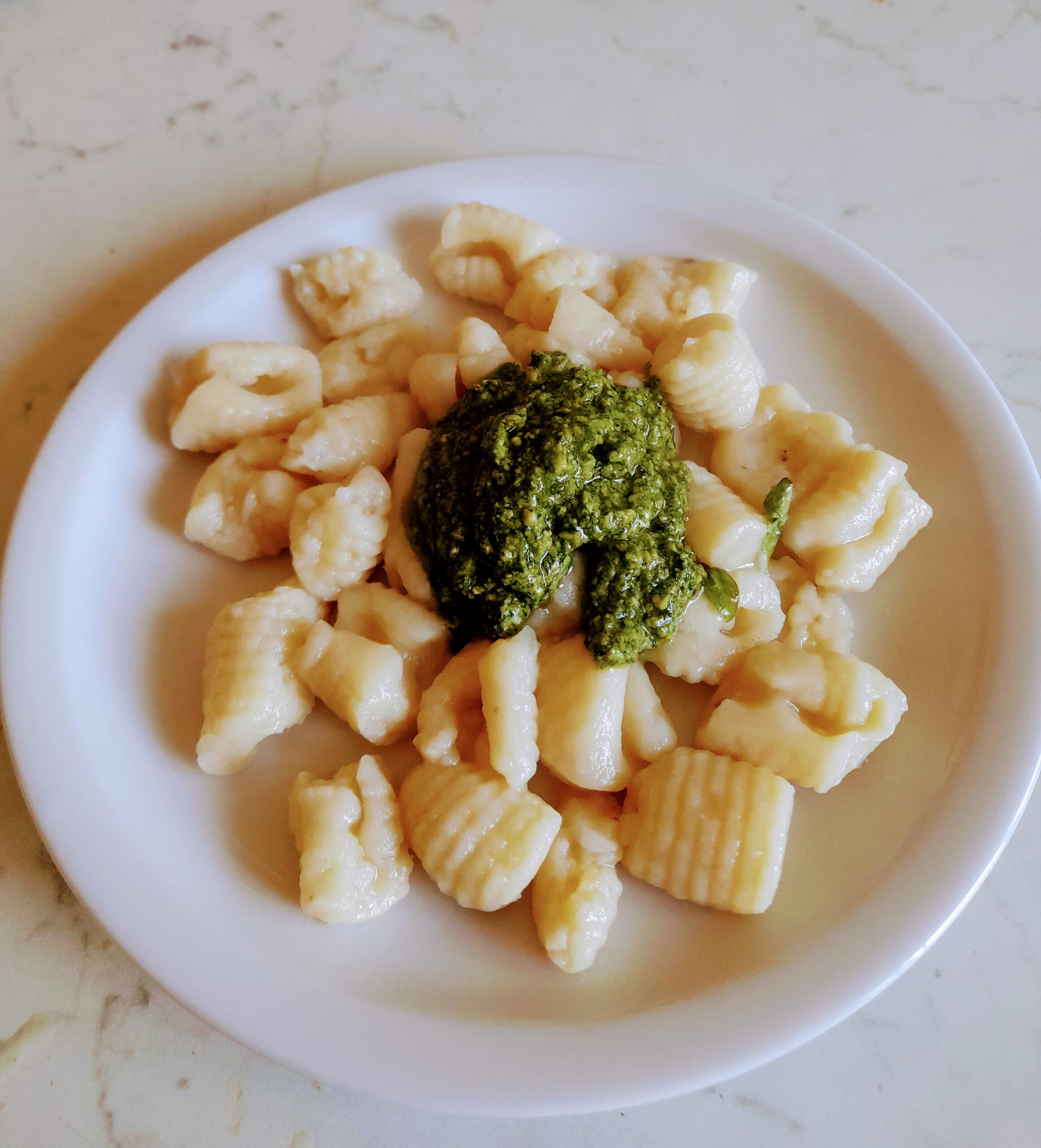 Plate of homemade gnocchi topped with fresh green pesto sauce on a white plate.