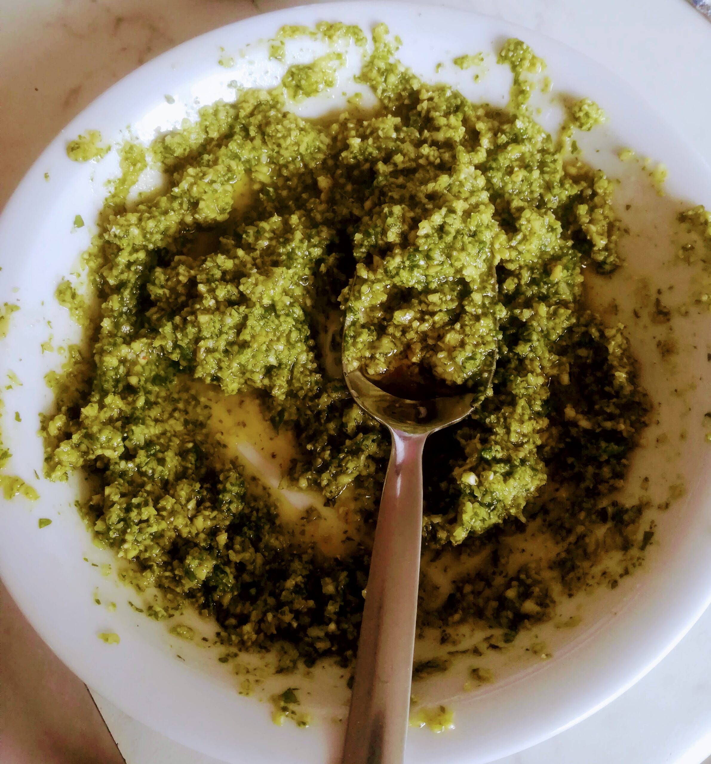Green pesto sauce in a white bowl with a spoon, perfect for pasta or sandwiches.