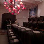 Barrels in a cozy room with a unique red chandelier and visitors, focused on wine or balsamic tasting experience.